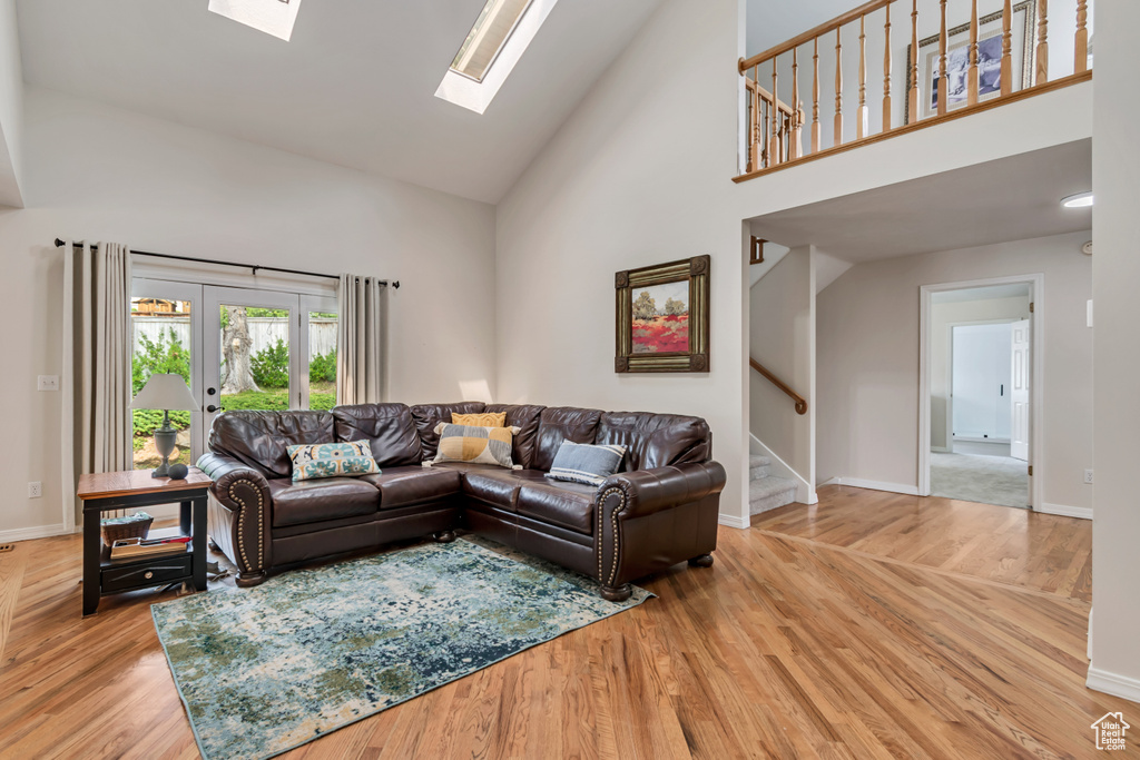 Living area with high vaulted ceiling, stairway, a skylight, light wood-type flooring, and baseboards