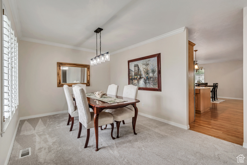 Dining room featuring light carpet, a chandelier, ornamental molding, and baseboards