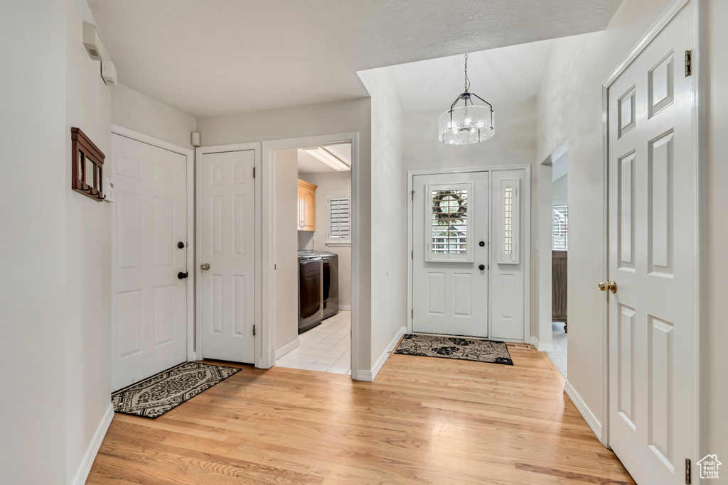 Entryway with washer / clothes dryer, a chandelier, light wood finished floors, and baseboards