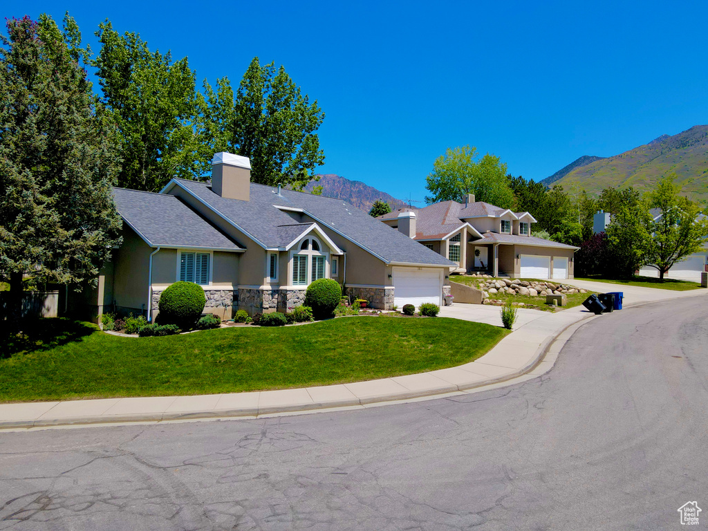 View of front of house with a mountain view, a garage, stone siding, and a front yard
