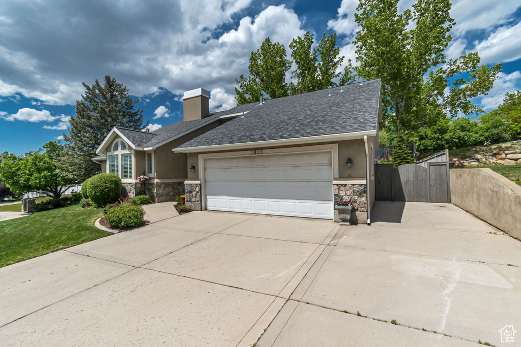 View of front of property featuring stone siding, concrete driveway, a gate, an attached garage, and stucco siding