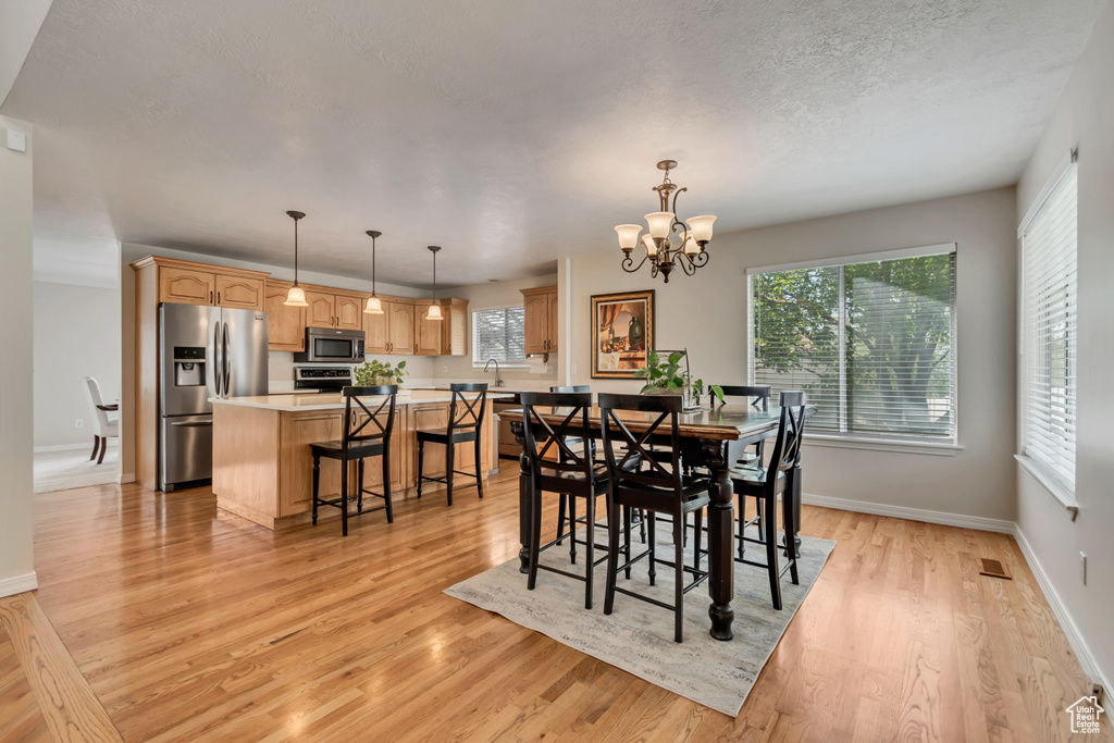Dining room featuring healthy amount of natural light, light wood-style floors, a chandelier, and baseboards