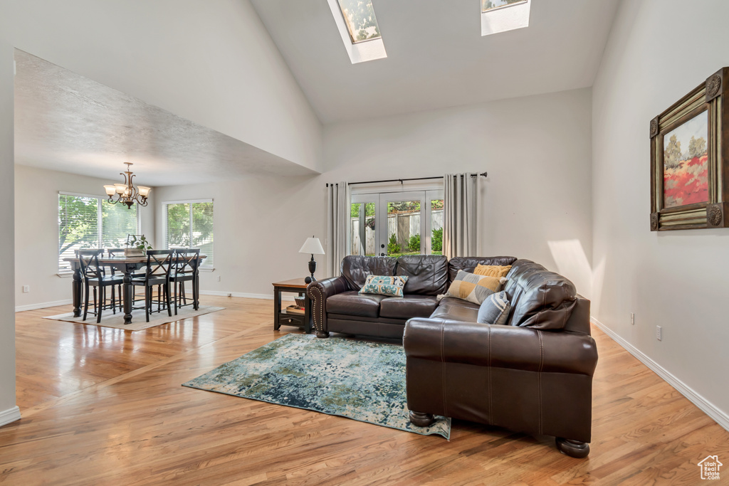 Living room with a chandelier, baseboards, light wood finished floors, high vaulted ceiling, and a skylight