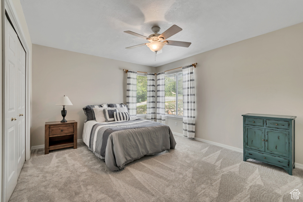 Bedroom with light colored carpet, baseboards, a ceiling fan, and a closet