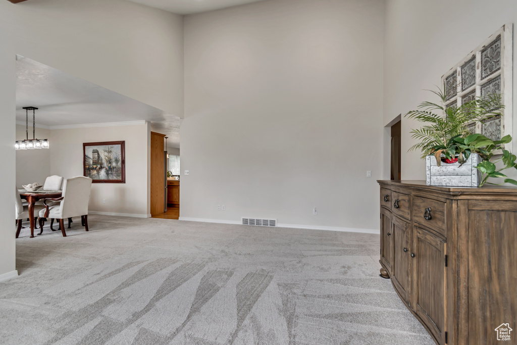 Living room with light carpet, baseboards, a towering ceiling, crown molding, and plenty of natural light