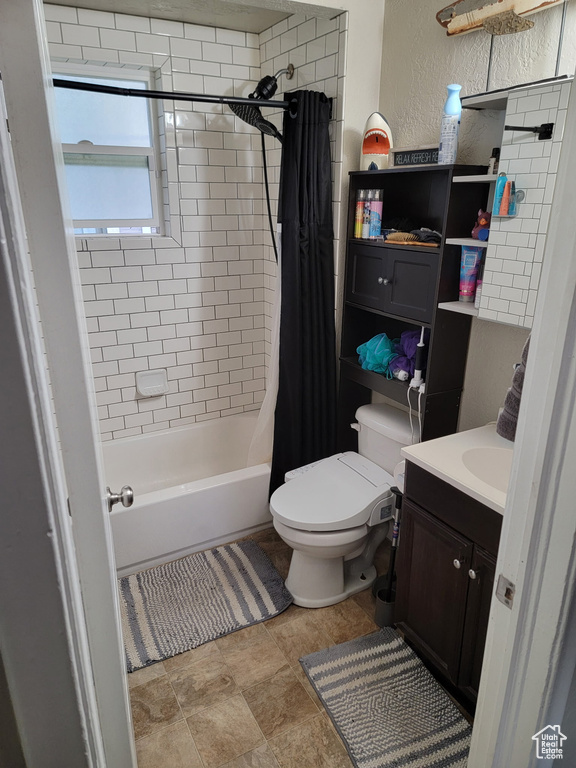 Bathroom with vanity, toilet, shower / bath combo, a textured wall, and stone finish floors