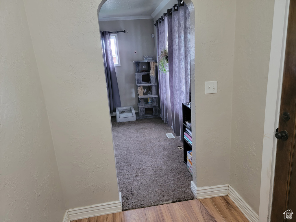 Hall with arched walkways, a textured wall, wood finished floors, crown molding, and baseboards