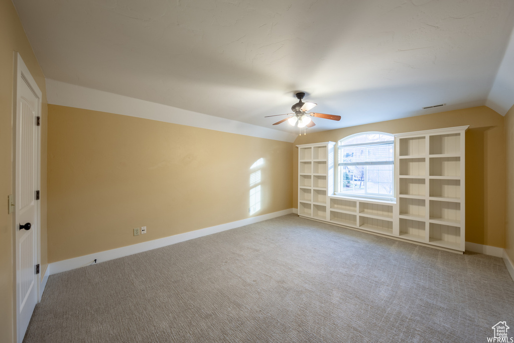 Empty room featuring a ceiling fan, carpet floors, baseboards, and vaulted ceiling