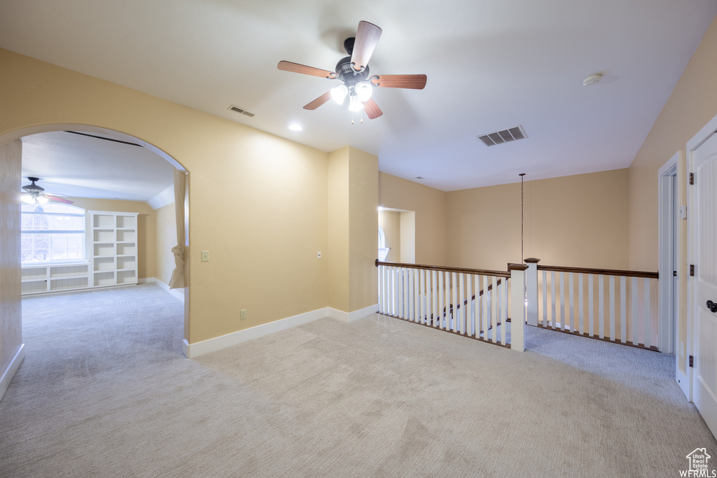 Carpeted empty room with a ceiling fan, arched walkways, a smoke detector, and baseboards