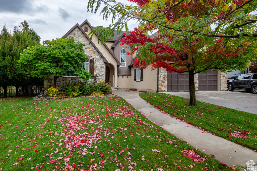 View of front of home featuring stone siding, driveway, stucco siding, a front yard, and a garage