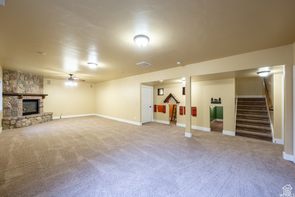 Finished basement featuring stairs, light colored carpet, a ceiling fan, and a stone fireplace