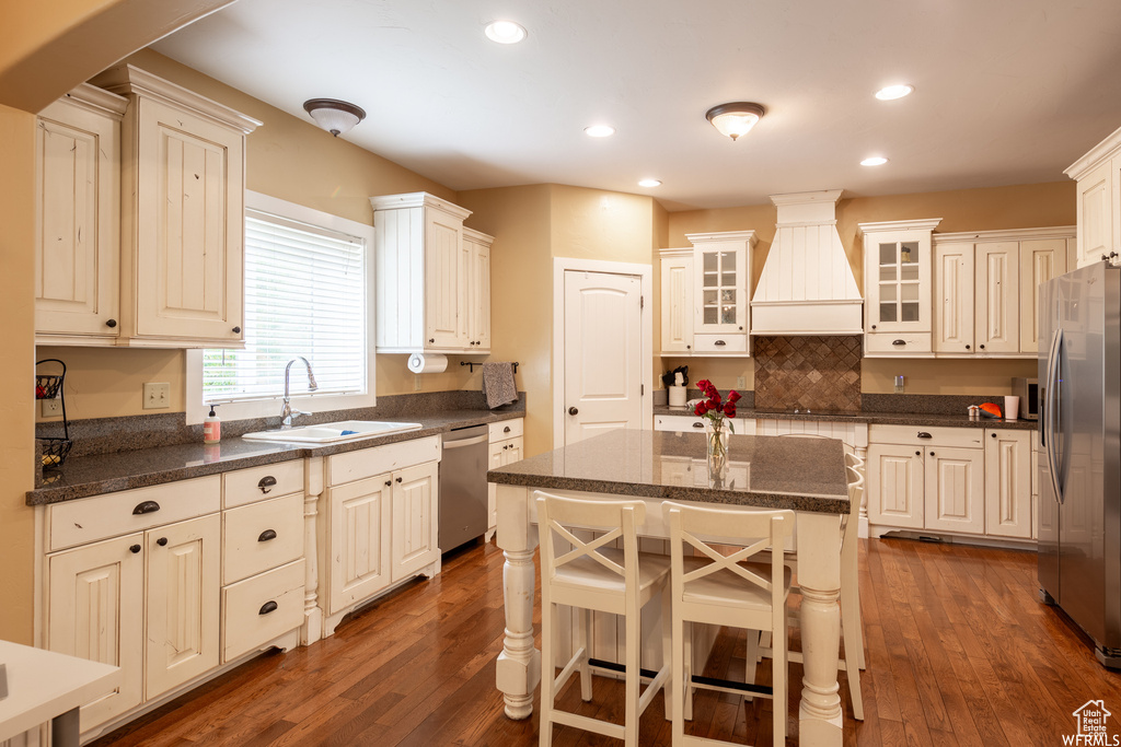 Kitchen with a sink, appliances with stainless steel finishes, custom exhaust hood, dark wood finished floors, and decorative backsplash
