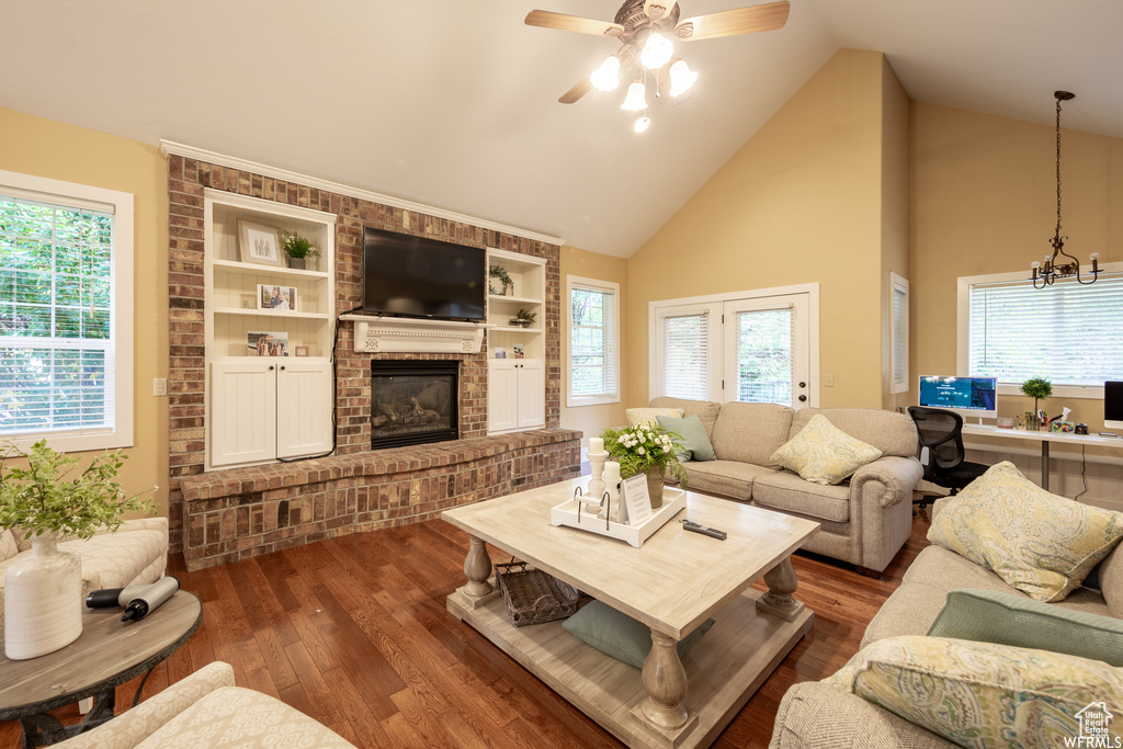 Living area with wood finished floors, a ceiling fan, a fireplace, a chandelier, and high vaulted ceiling