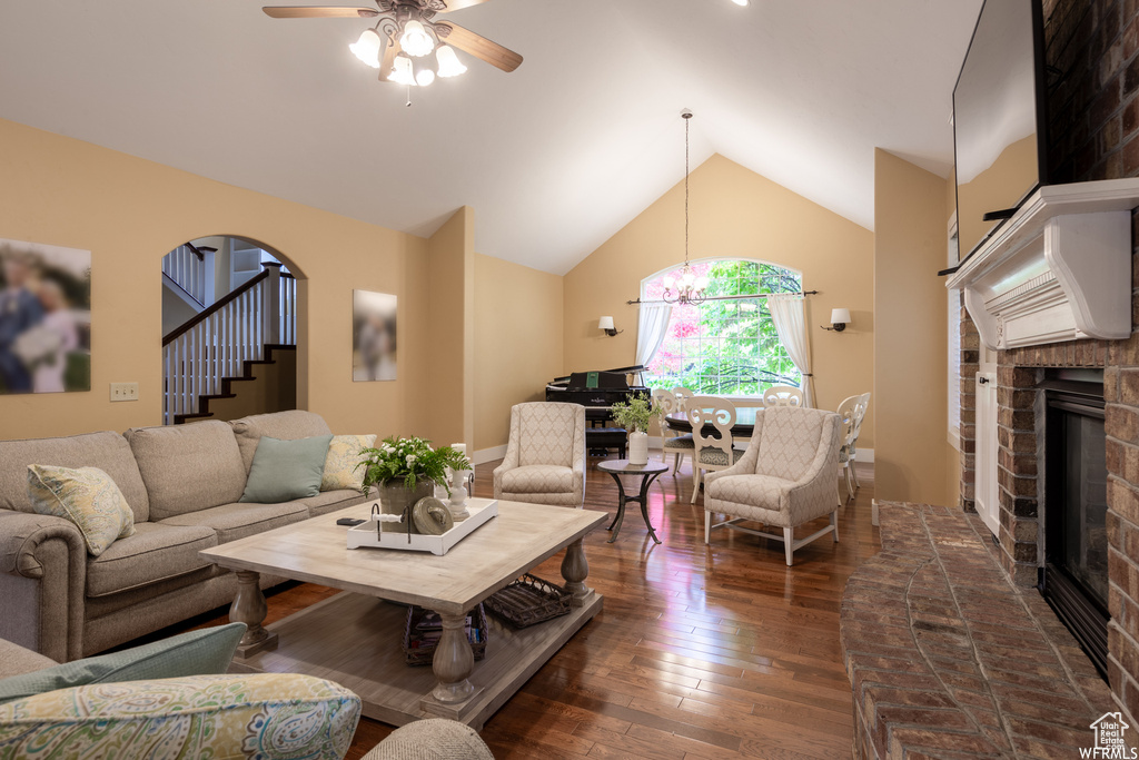 Living area featuring a brick fireplace, dark wood-type flooring, ceiling fan, stairway, and high vaulted ceiling