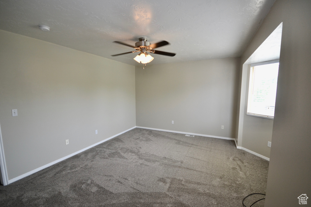 Carpeted empty room featuring a ceiling fan, baseboards, and a smoke detector