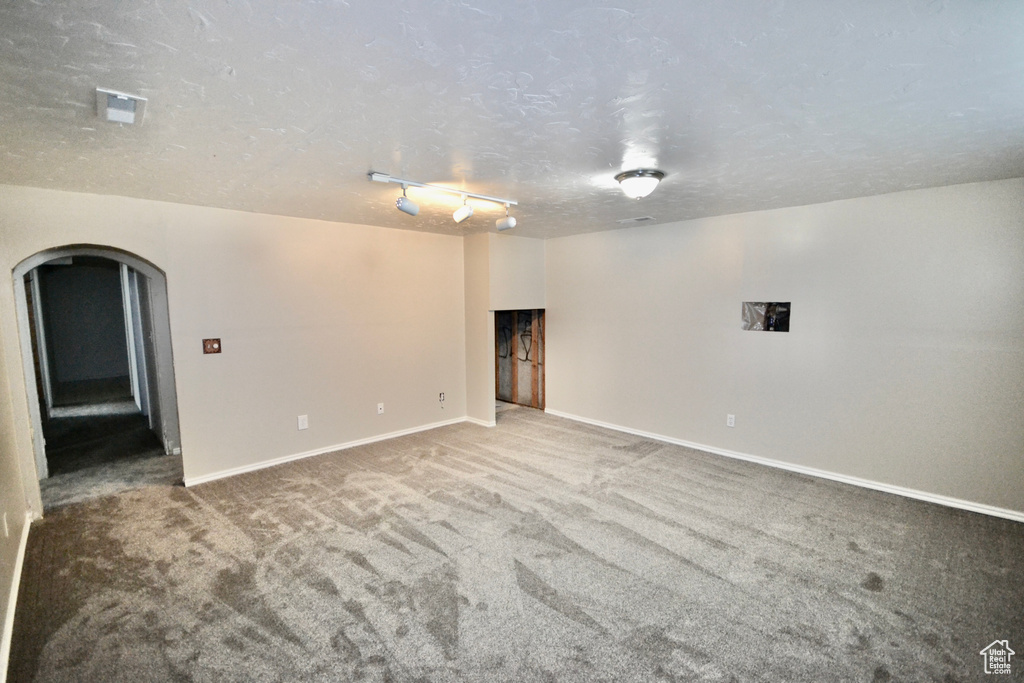 Empty room with arched walkways, carpet floors, baseboards, and a textured ceiling