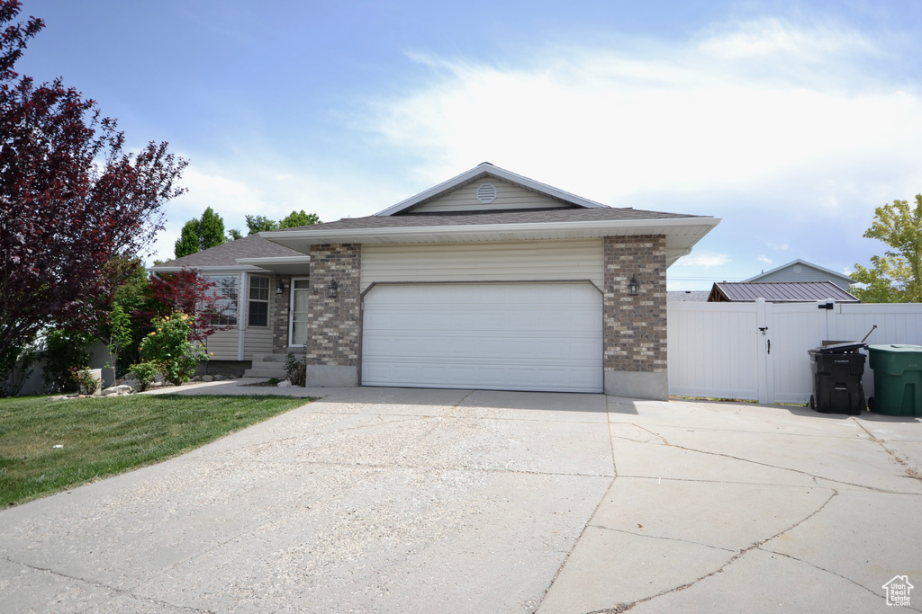 Ranch-style home featuring brick siding, concrete driveway, an attached garage, and a gate