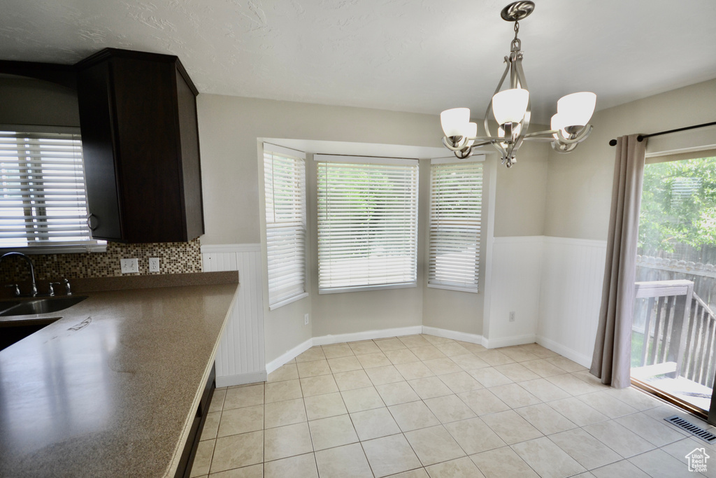 Unfurnished dining area with a sink, a chandelier, a wainscoted wall, and light tile patterned floors