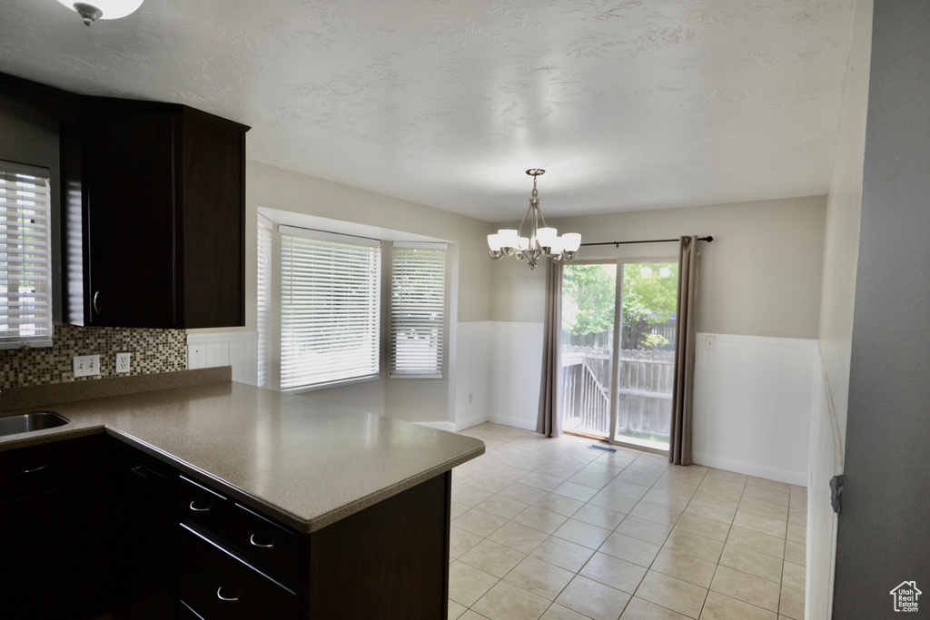 Kitchen with wainscoting, a chandelier, a sink, light tile patterned floors, and a peninsula