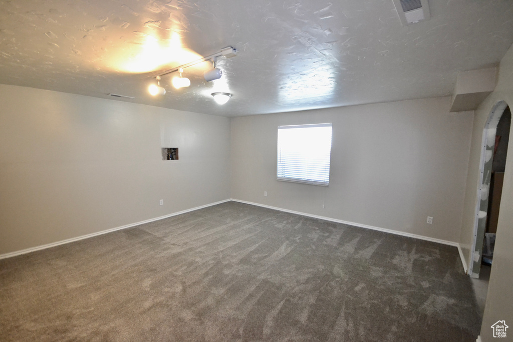 Below grade area featuring dark carpet, baseboards, a textured ceiling, and rail lighting