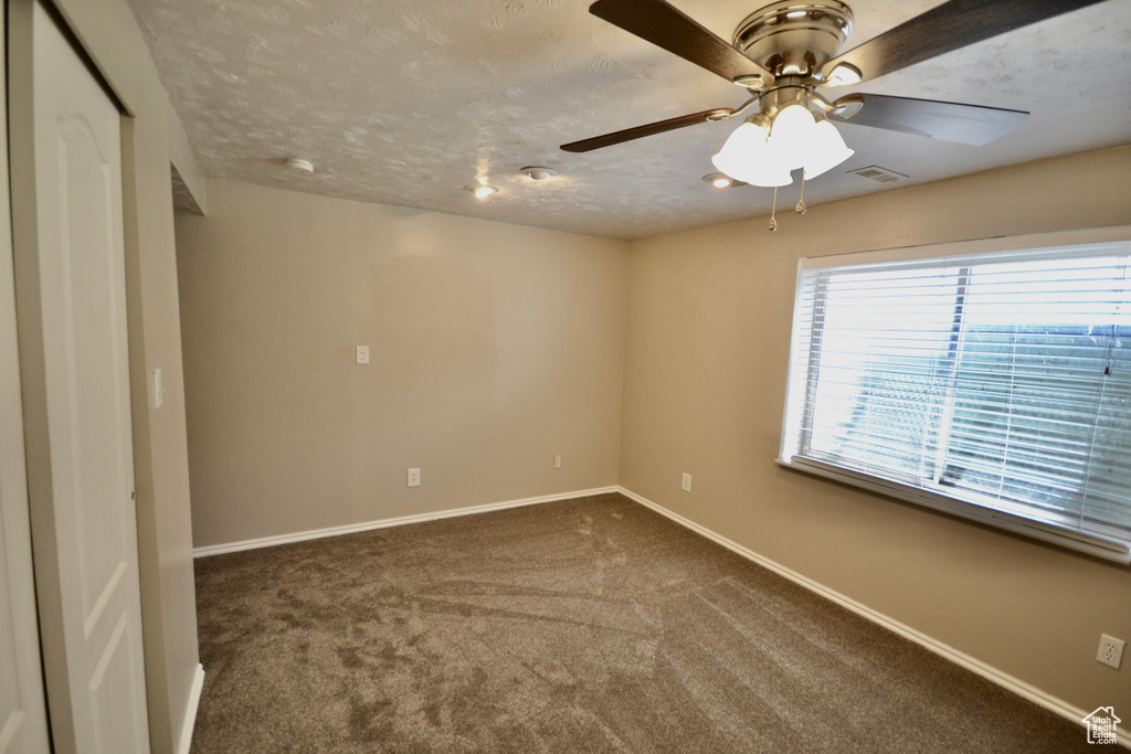 Spare room featuring baseboards, a ceiling fan, dark carpet, and a textured ceiling