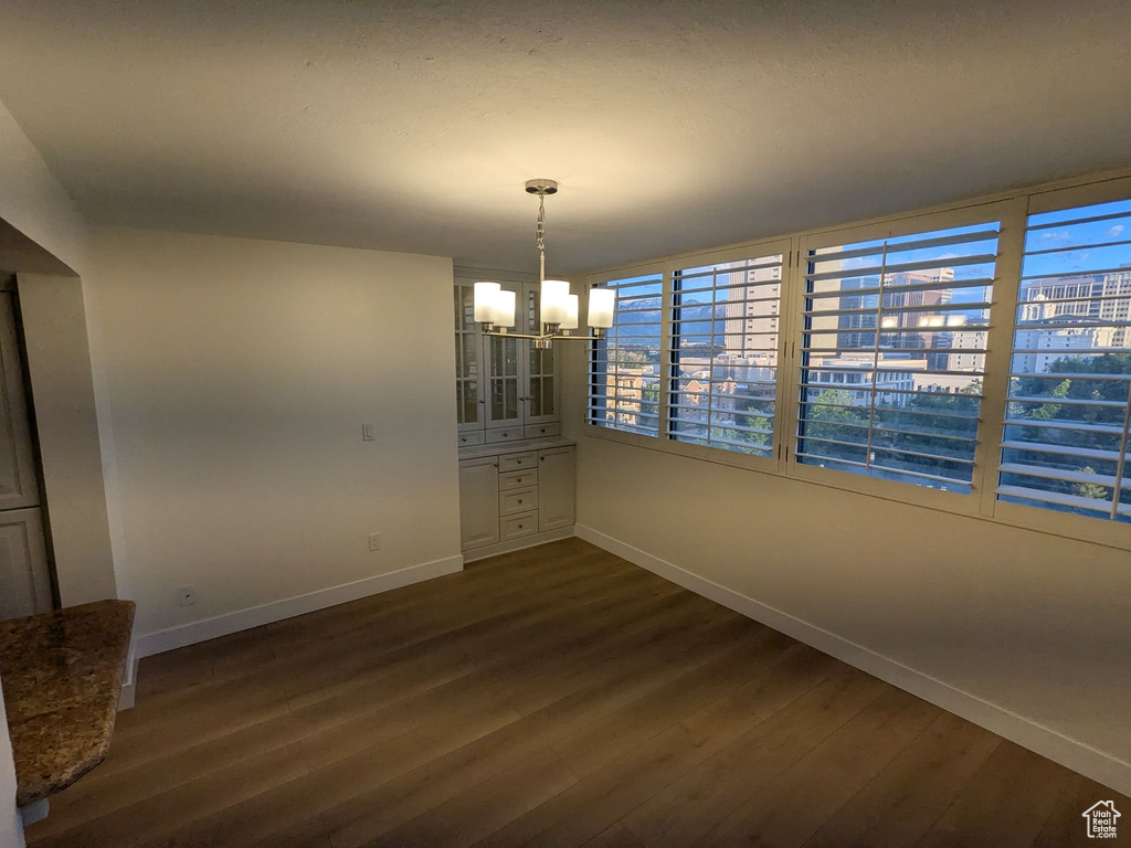 Unfurnished dining area featuring baseboards, a chandelier, and dark wood finished floors