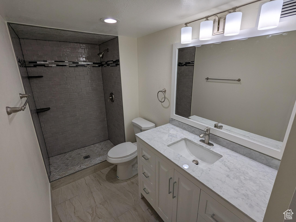 Full bathroom featuring toilet, tiled shower, vanity, marble finish flooring, and recessed lighting