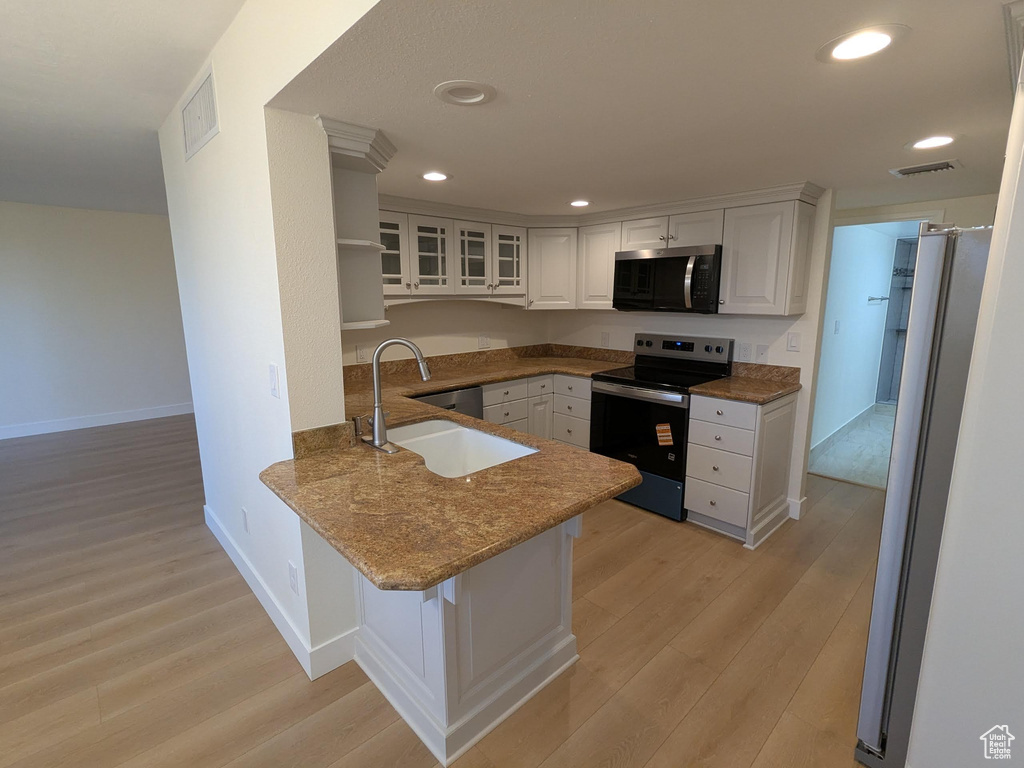 Kitchen featuring appliances with stainless steel finishes, a peninsula, light wood finished floors, white cabinetry, and a sink