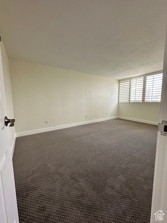 Spare room featuring dark carpet and baseboards