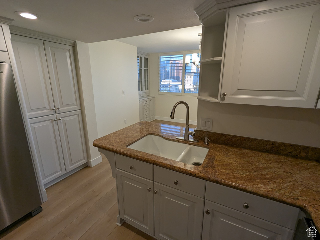 Kitchen featuring freestanding refrigerator, a sink, light wood-type flooring, recessed lighting, and white cabinetry