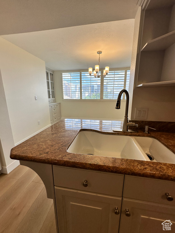 Kitchen with a sink, dark stone countertops, a chandelier, baseboards, and open shelves