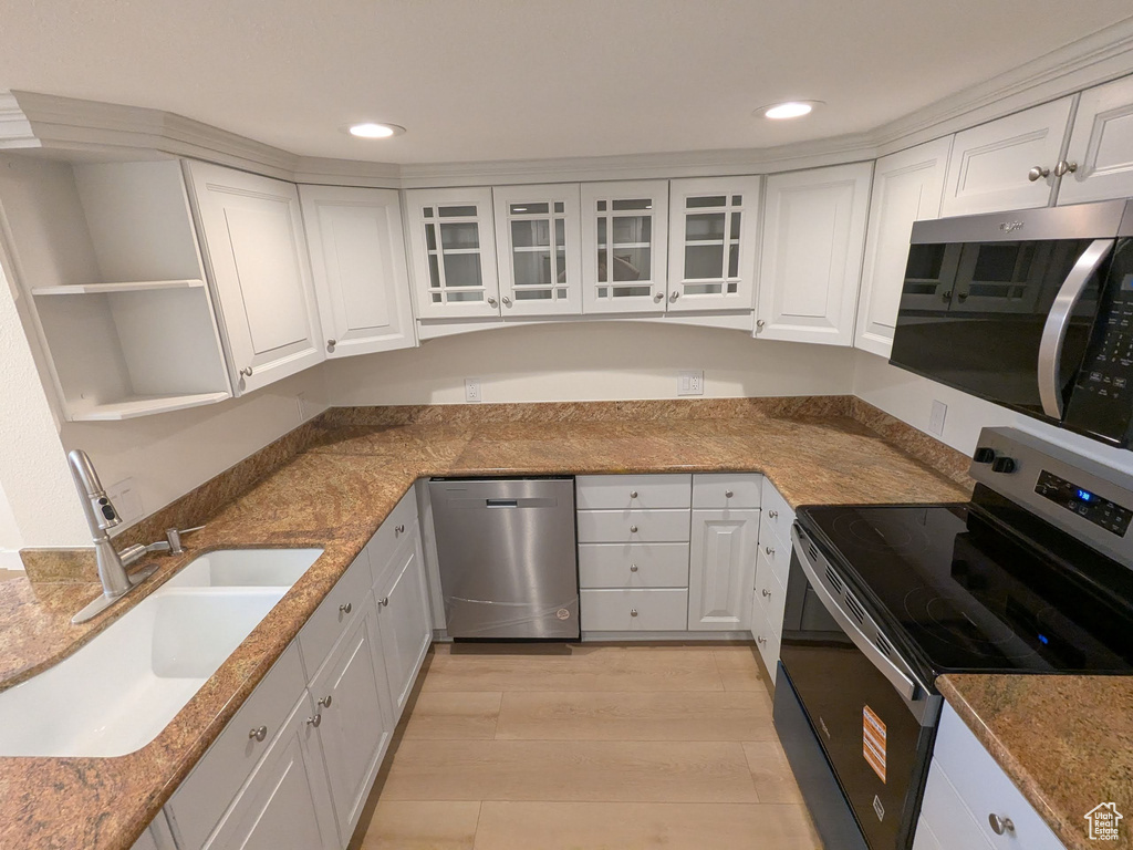 Kitchen featuring stainless steel appliances, a sink, white cabinets, light wood finished floors, and recessed lighting