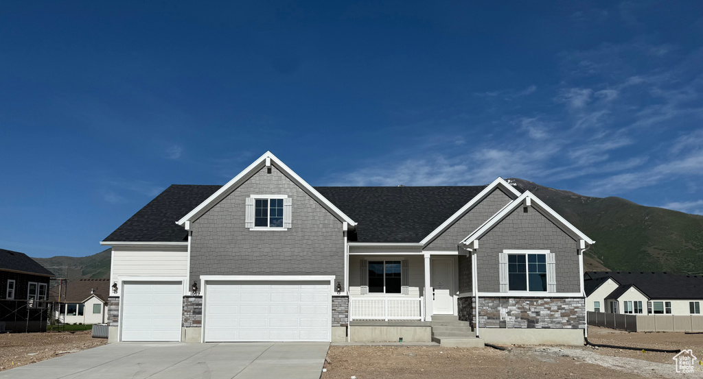 Craftsman house featuring a porch, stone siding, an attached garage, a mountain view, and concrete driveway