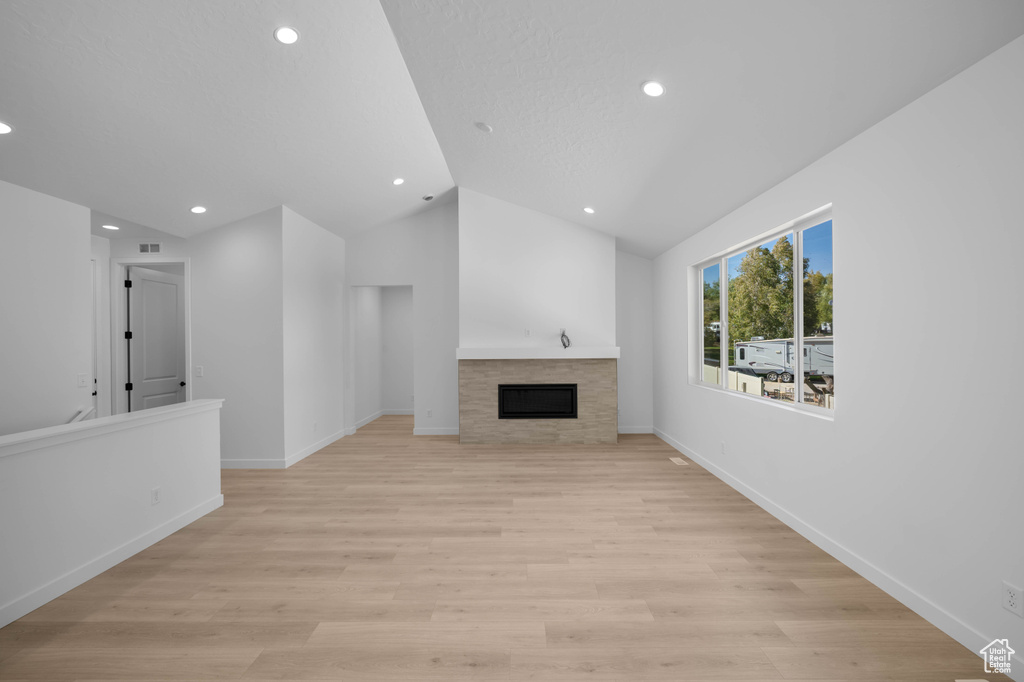 Unfurnished living room featuring recessed lighting, vaulted ceiling, a tiled fireplace, light wood finished floors, and baseboards