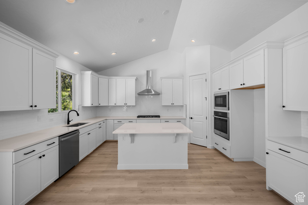 Kitchen with stainless steel appliances, wall chimney exhaust hood, a sink, a center island, and white cabinets
