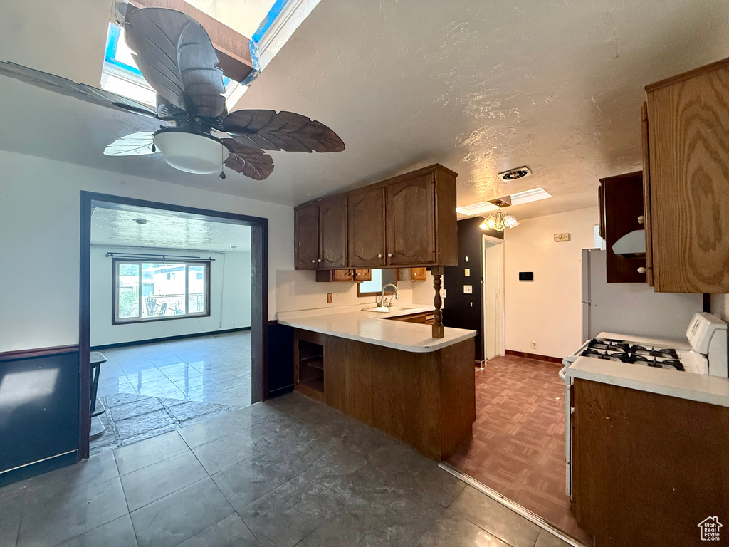 Kitchen with a sink, light countertops, ceiling fan, a peninsula, and range with gas stovetop