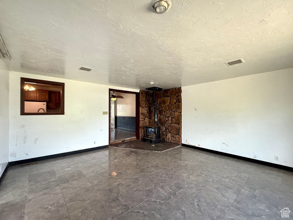 Unfurnished living room featuring a wood stove, baseboards, and a textured ceiling