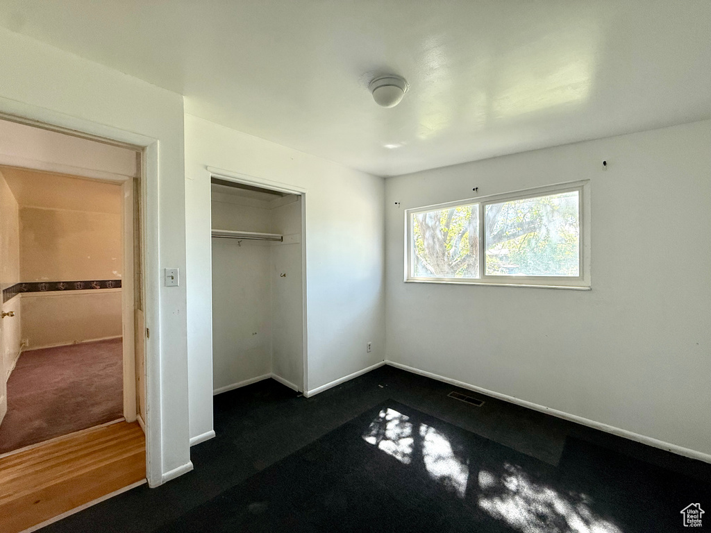 Unfurnished bedroom featuring dark carpet, baseboards, and a closet