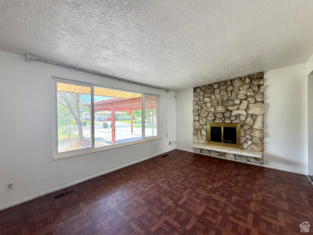 Unfurnished living room featuring a textured ceiling, a stone fireplace, and baseboards