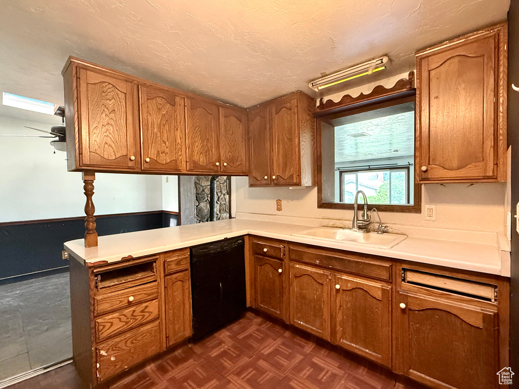 Kitchen with a sink, black dishwasher, brown cabinetry, light countertops, and a peninsula