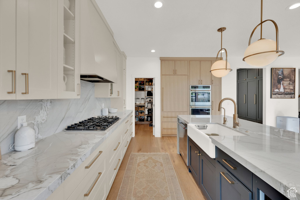 Kitchen with appliances with stainless steel finishes, light wood finished floors, light stone counters, a sink, and decorative backsplash
