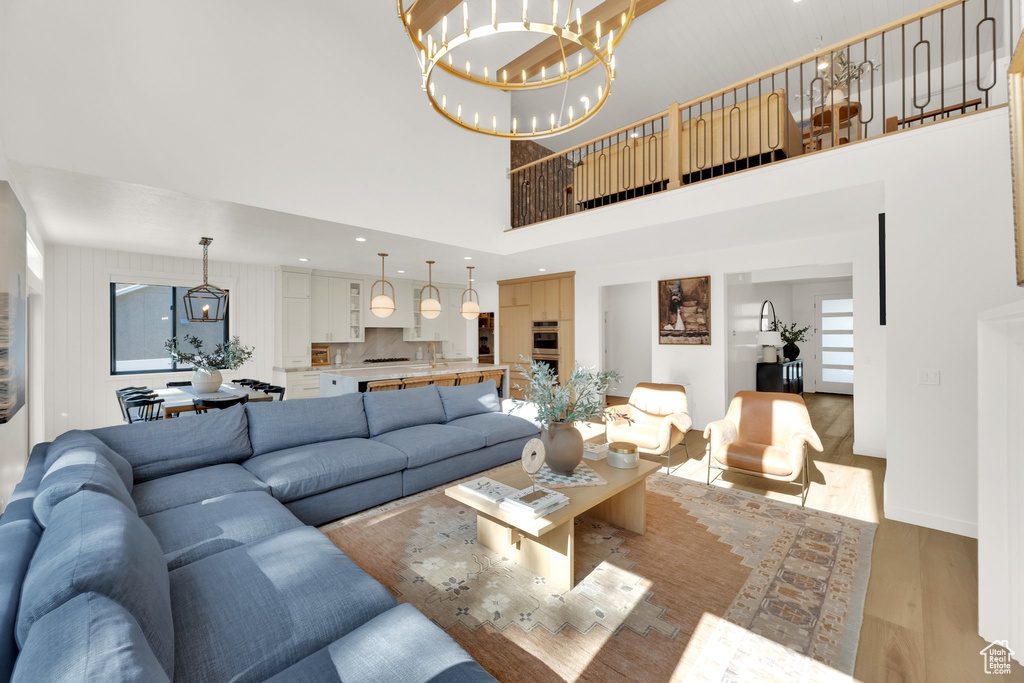 Living room featuring light wood-style flooring, a chandelier, a high ceiling, and baseboards