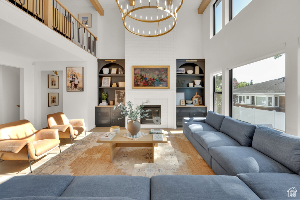 Living room with a high ceiling, built in shelves, a chandelier, a glass covered fireplace, and wood finished floors