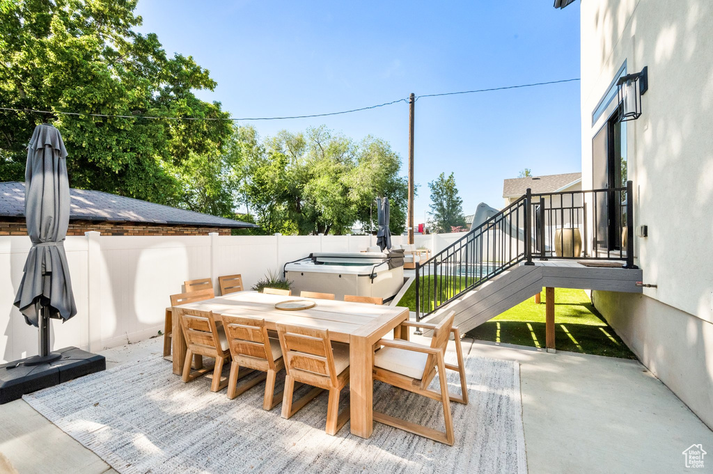 Wooden terrace featuring outdoor dining area, a hot tub, a fenced backyard, and a patio