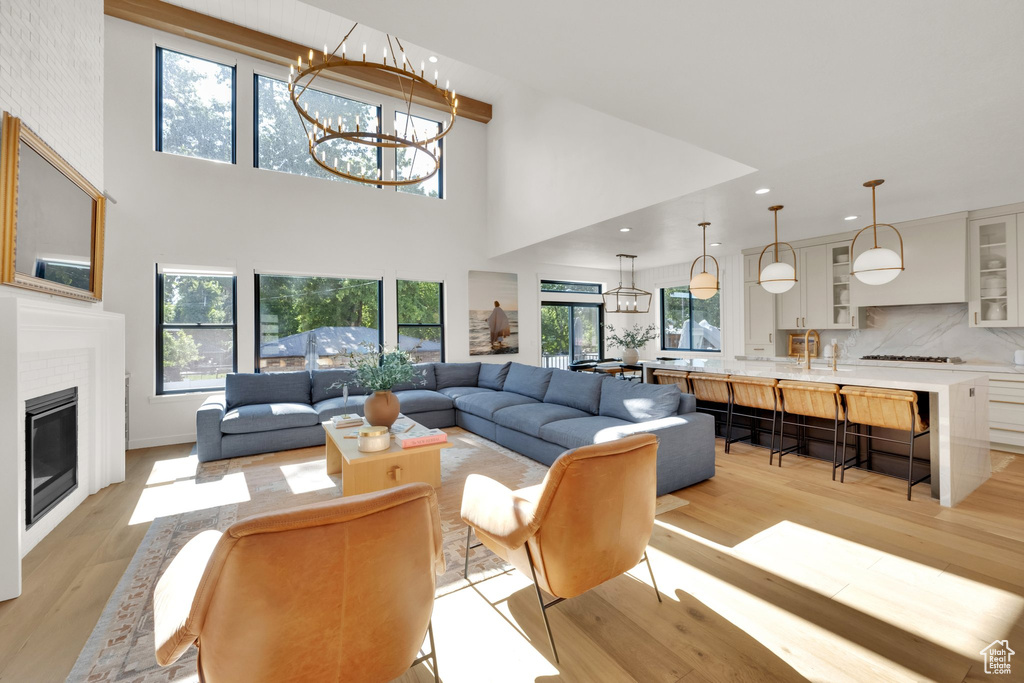 Living area featuring light wood-style flooring, healthy amount of natural light, recessed lighting, a towering ceiling, and a glass covered fireplace