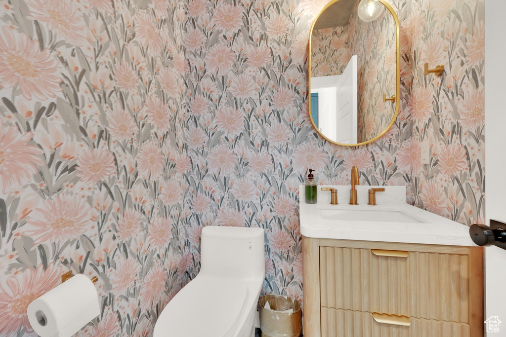 Half bathroom with wallpapered walls, vanity, and toilet