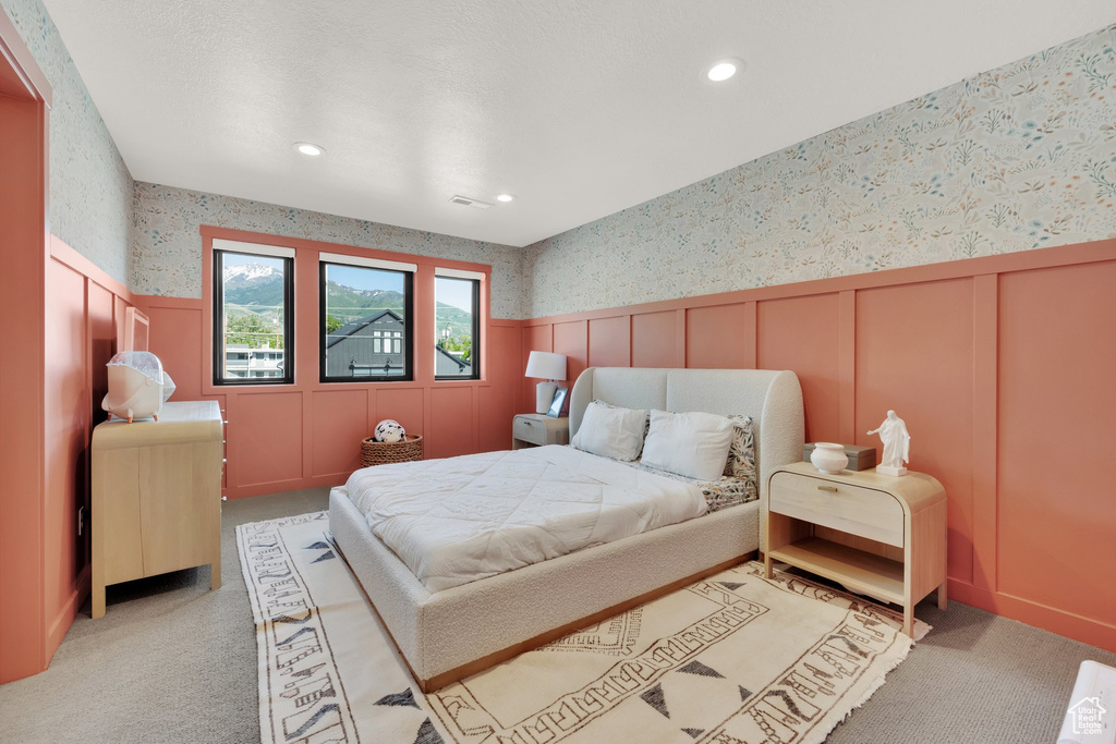 Bedroom featuring wallpapered walls, light colored carpet, a decorative wall, recessed lighting, and wainscoting