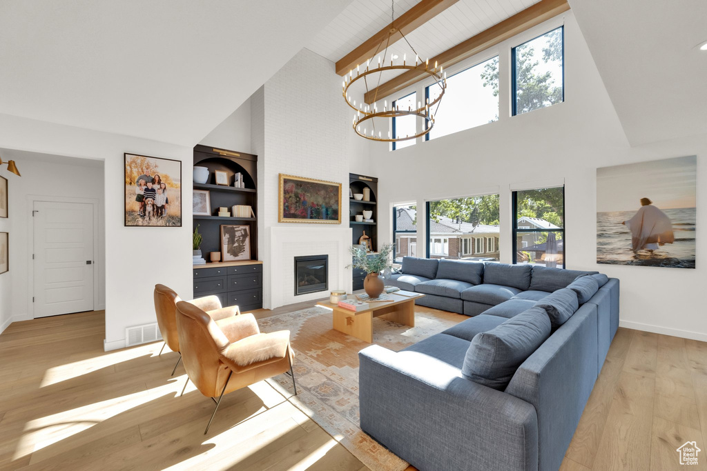 Living room featuring high vaulted ceiling, light wood-style flooring, baseboards, a glass covered fireplace, and beam ceiling