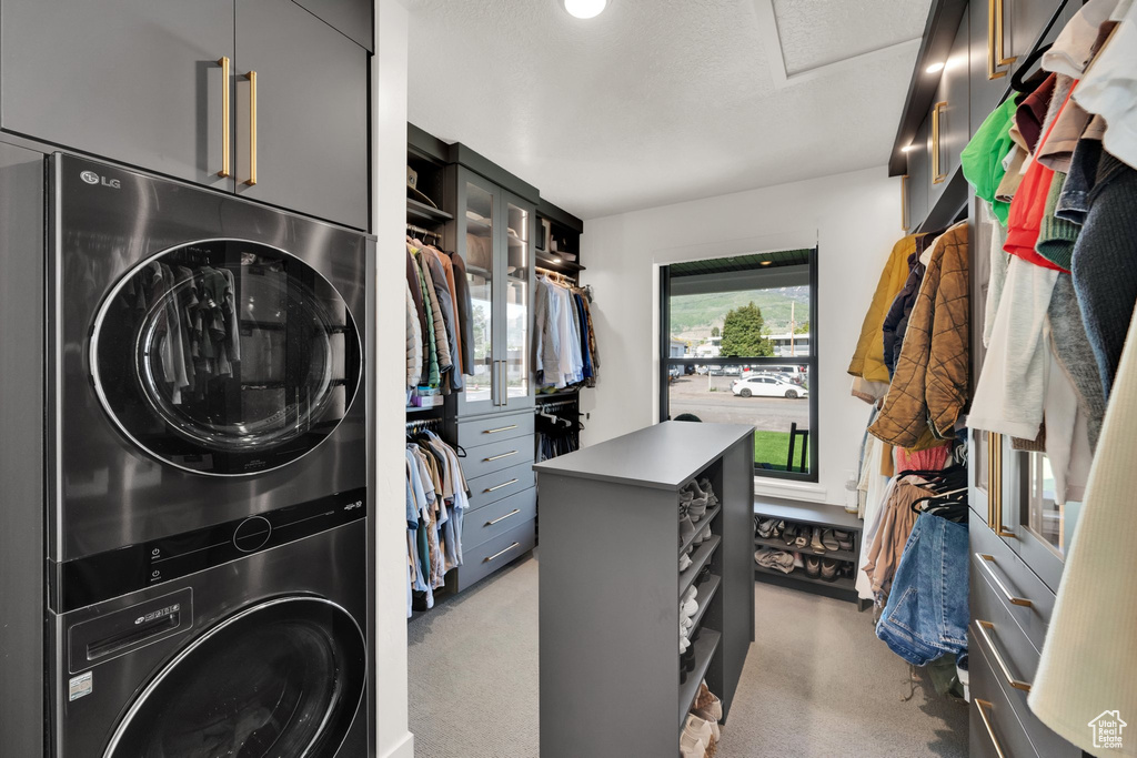 Laundry room featuring stacked washer and clothes dryer, light carpet, and attic access