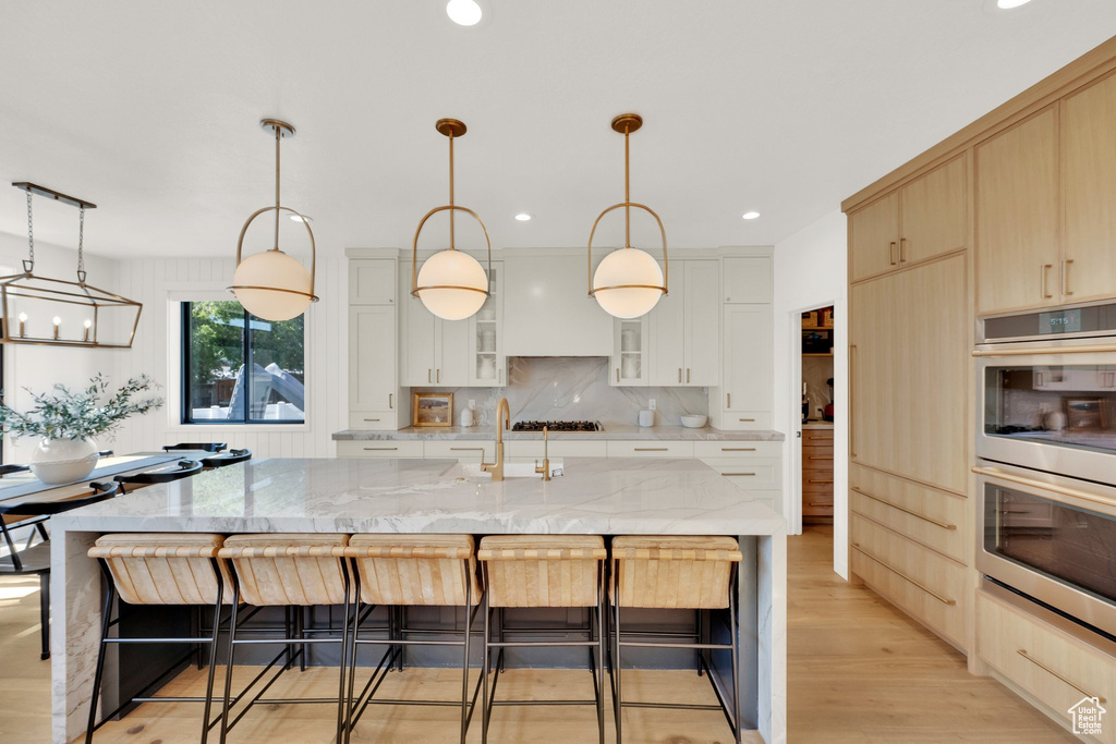 Kitchen with double oven, a sink, a kitchen bar, glass insert cabinets, and light stone counters